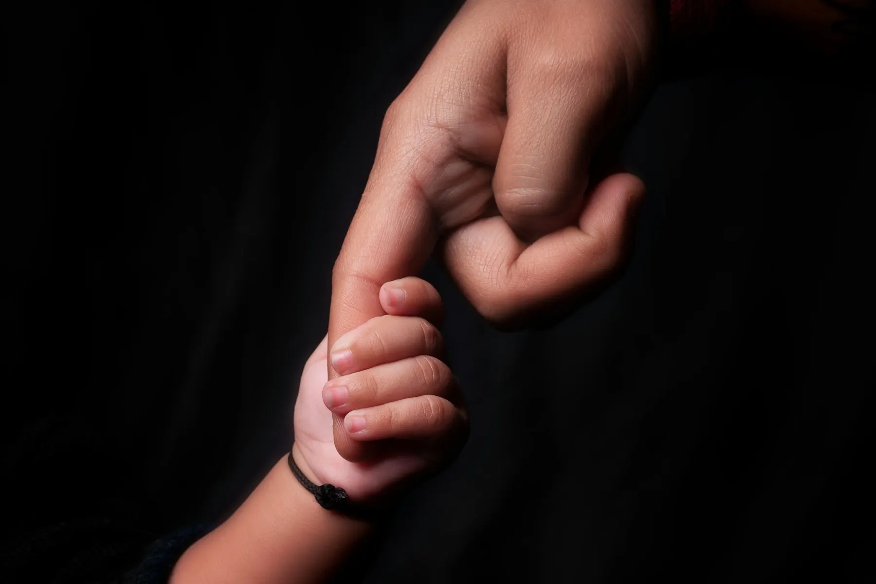 La mano de un niño pequeño sujetando el dedo de un adulto, sobre un fondo oscuro.