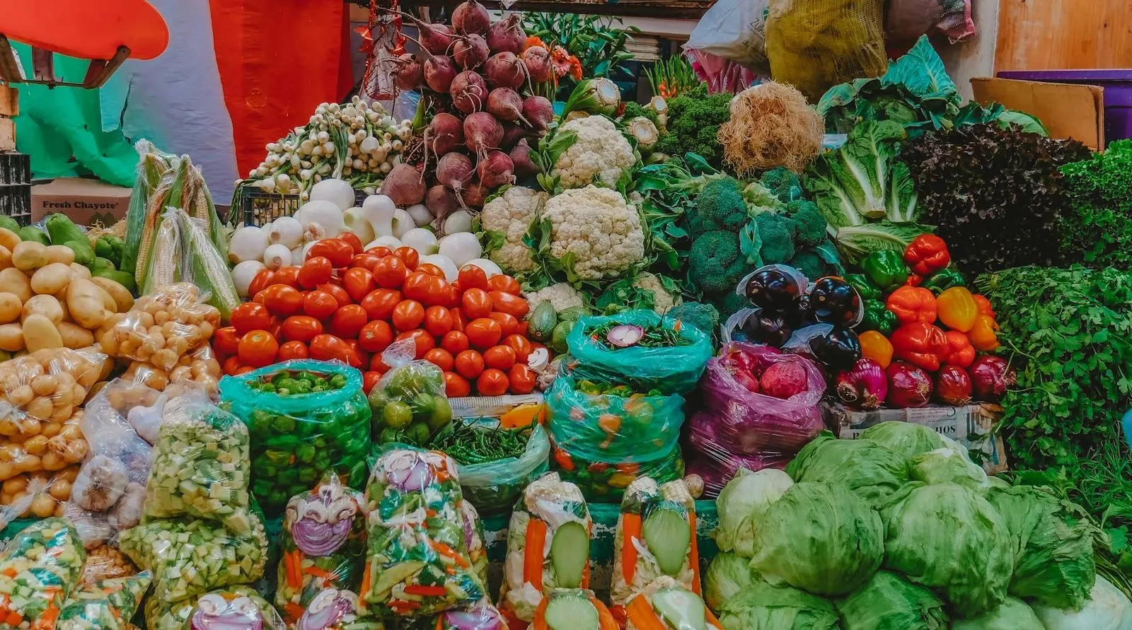 Un mercado mexicano con puestos de verduras, chiles secos y especias en canastas de mimbre.