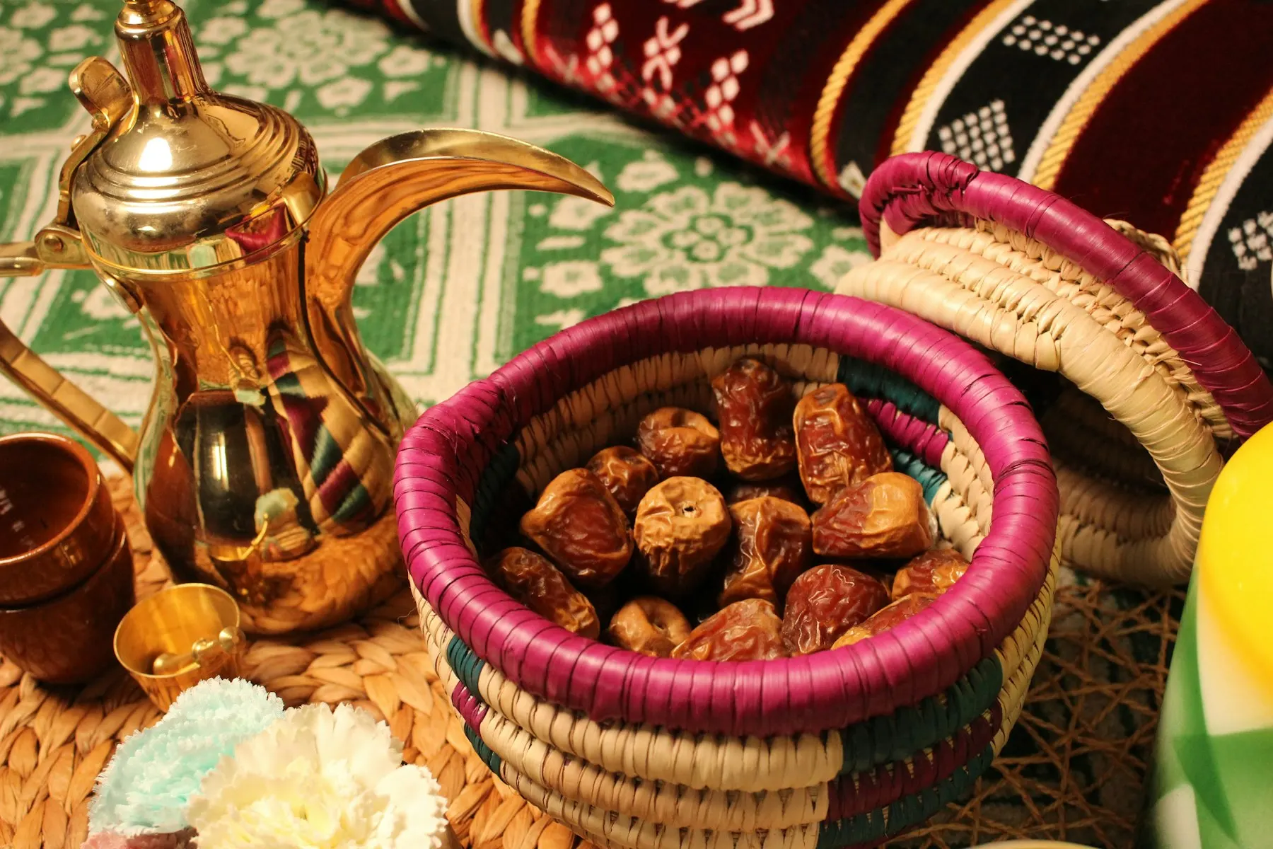 Una cesta de dátiles junto a una cafetera árabe sobre un tapiz de colores, lista para el iftar.