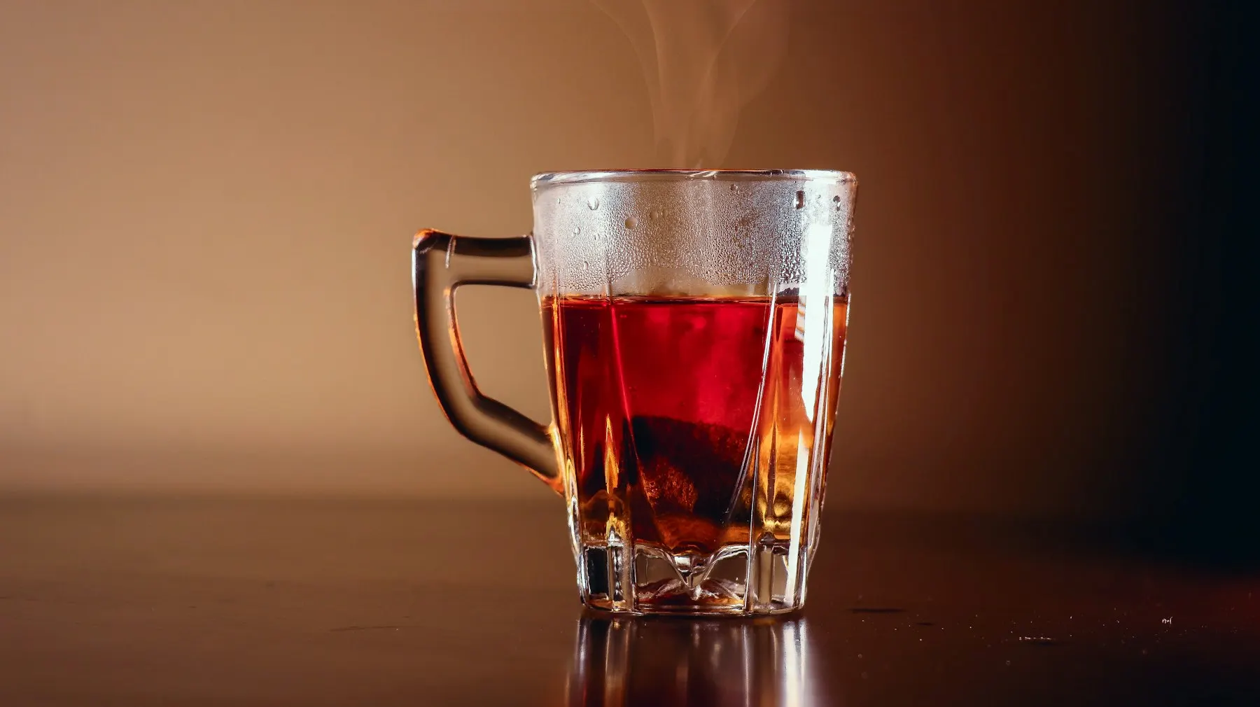 Un vaso de té caliente con vapor sobre una mesa de madera, listo para ofrecer a una visita.