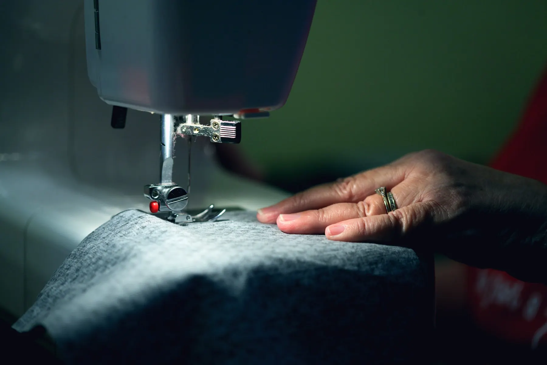 Unas manos cosen tela con una máquina de coser, en un ambiente cálido de taller.