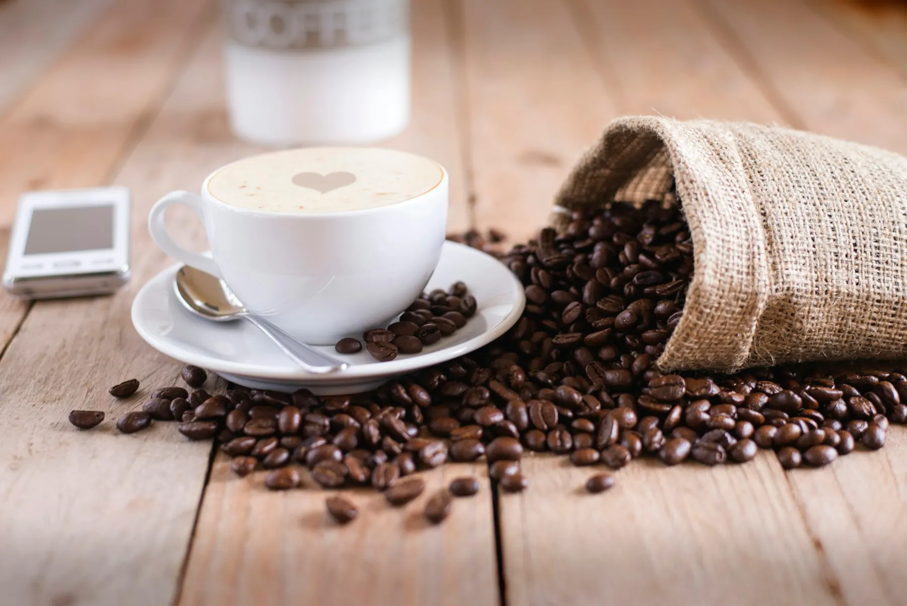 Granos de café tostados y una taza humeante sobre una mesa de madera.