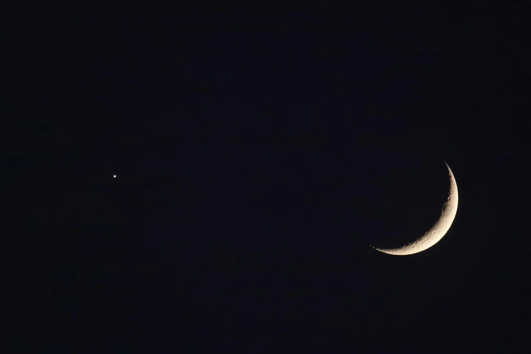 Una luna creciente delgada sobre el cielo del atardecer, apenas visible tras el horizonte.