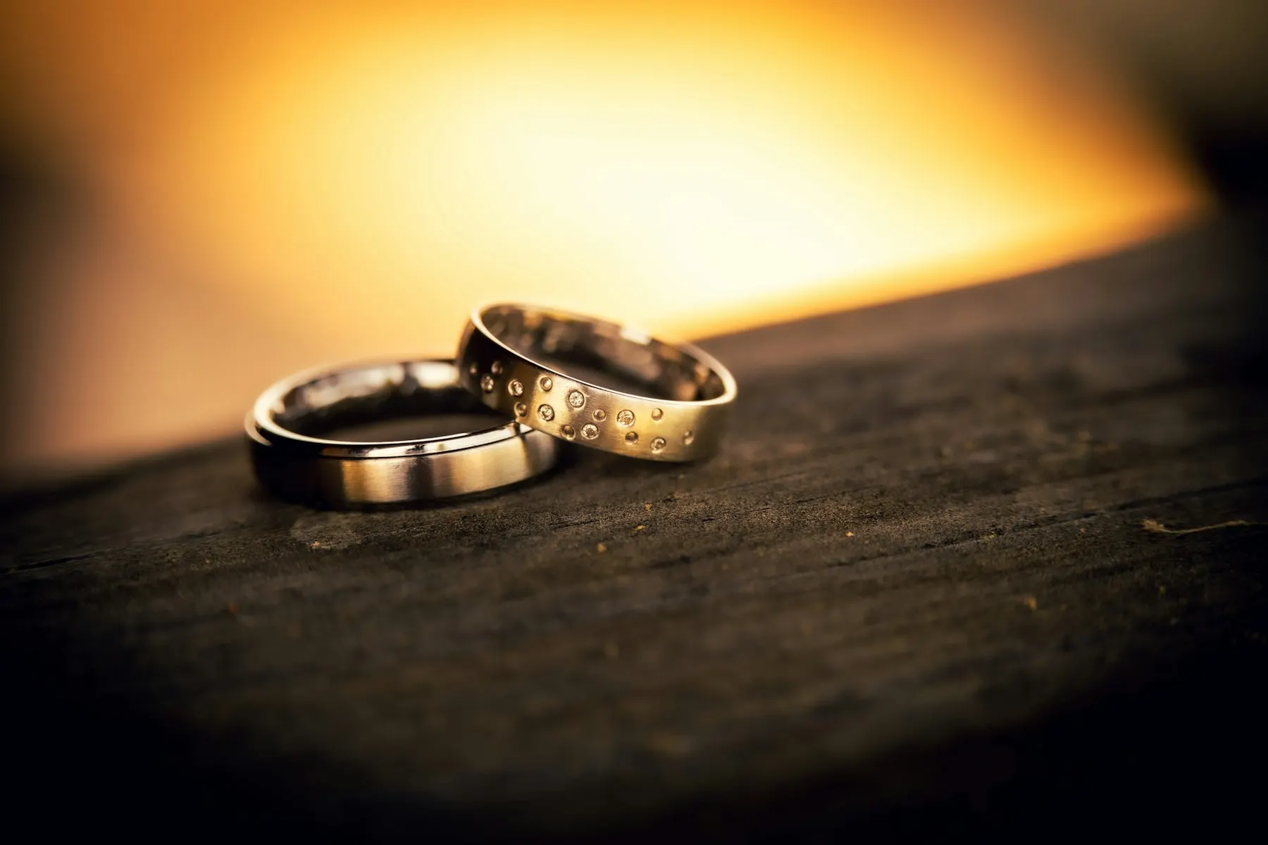 Dos anillos de matrimonio apoyados sobre una mesa de madera, con luz cálida de fondo.