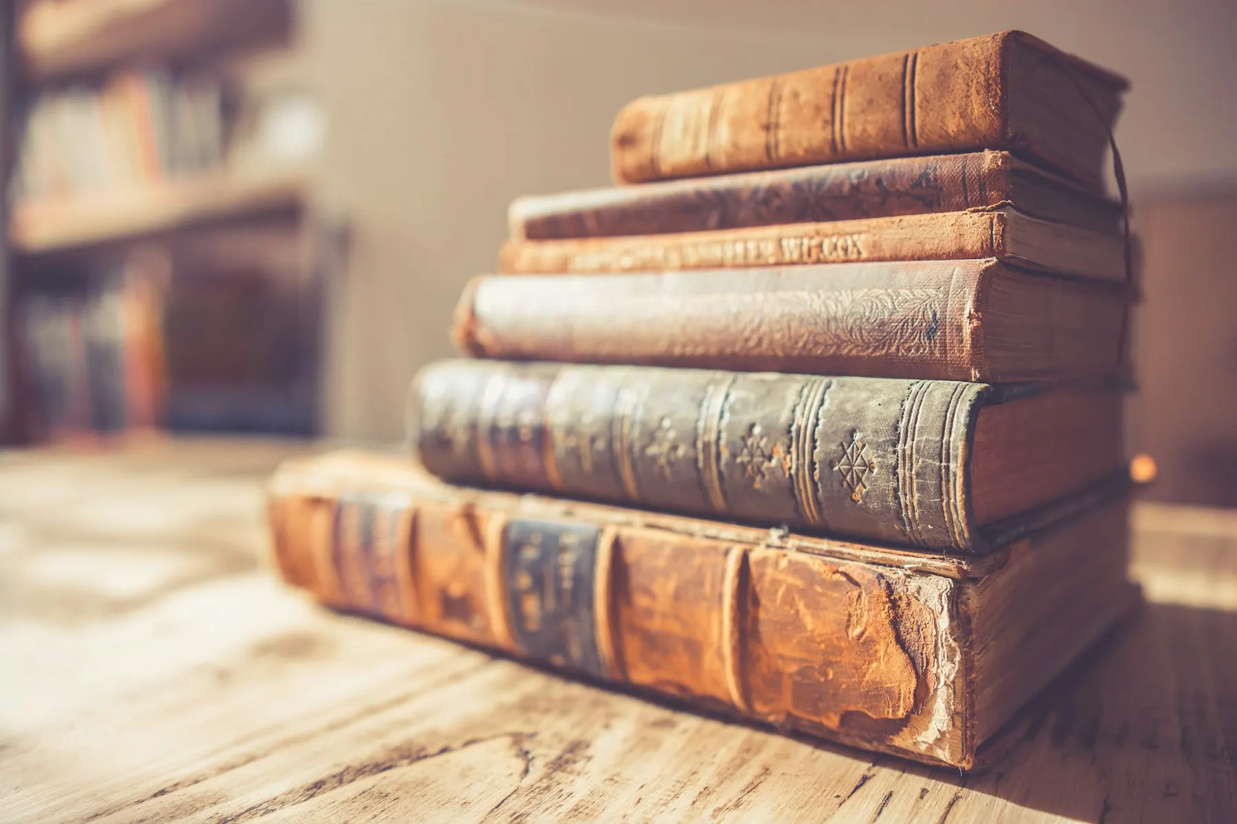 Pilas de libros antiguos encuadernados en cuero sobre una mesa de madera.