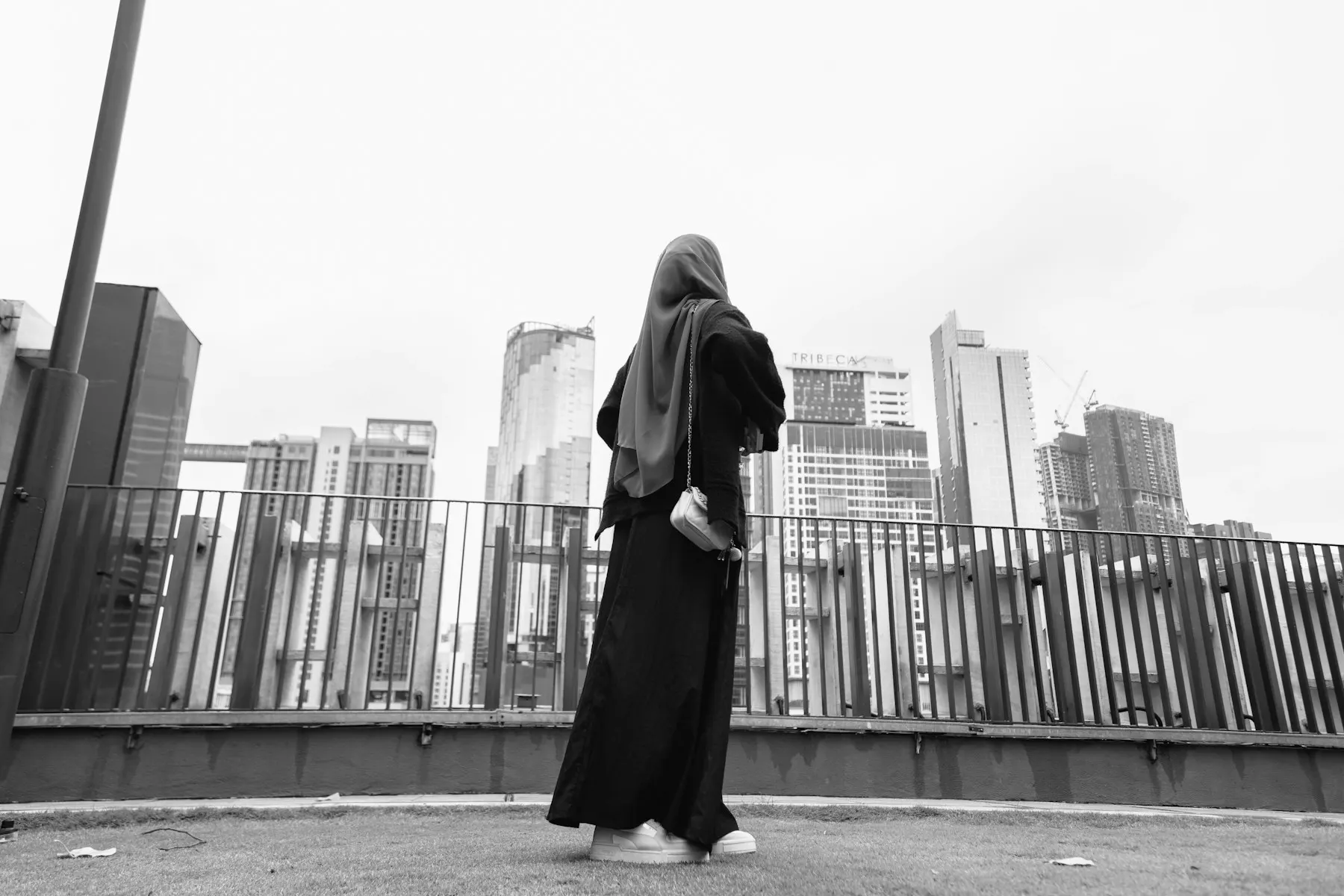 Una mujer con hiyab y abaya camina por un puente con la ciudad al fondo.
