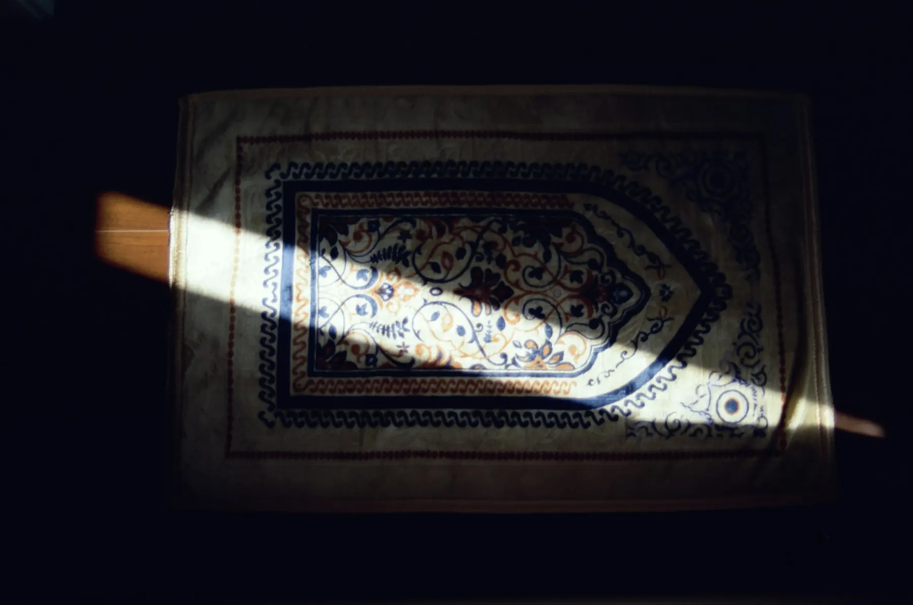 Un tapete de oración extendido junto a una ventana con luz cálida de tarde, sin personas.