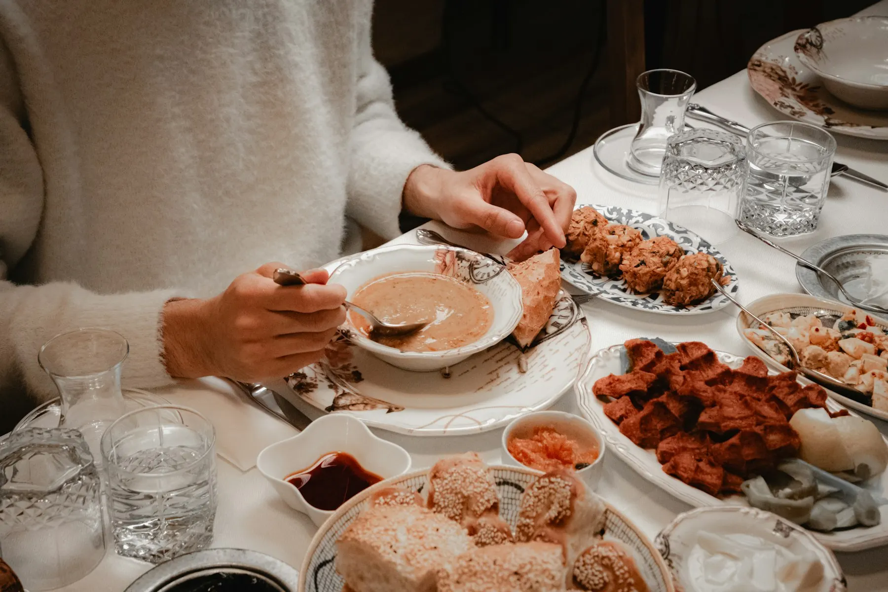 Manos de una familia comparten platos en una mesa puesta con luz cálida.