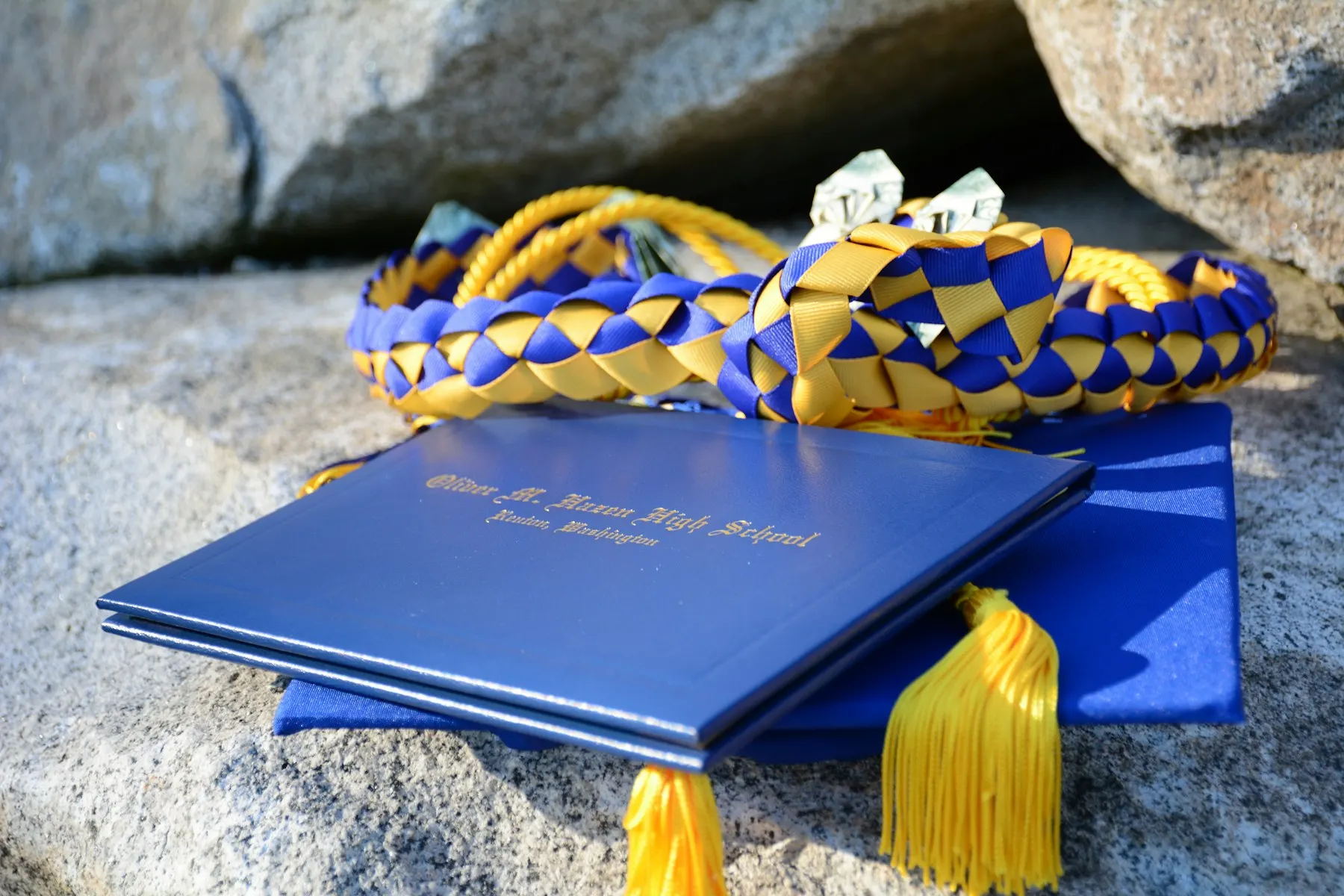 Un libro azul con un borlas amarillo encima, símbolo de graduación, sobre una roca.