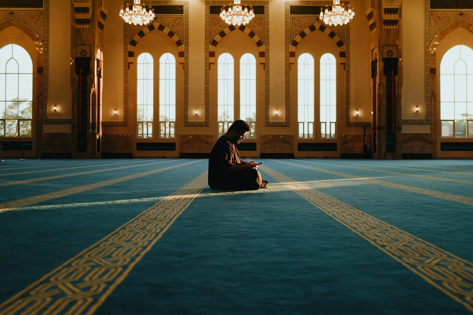 Una mujer reza sola sobre la alfombra verde de una gran mezquita, vista de espaldas.