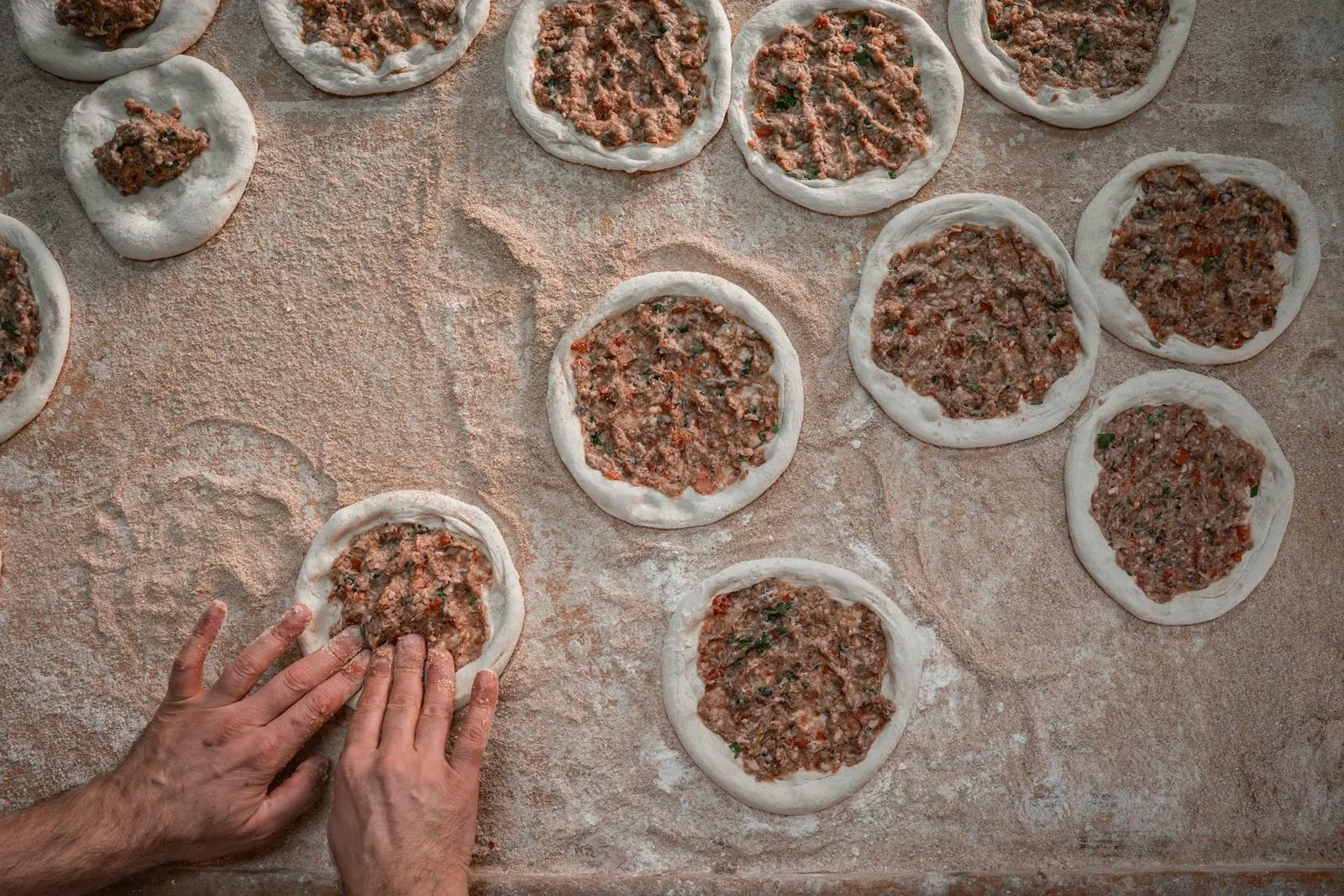 Unas manos preparan pequeños empanadillas de masa sobre una mesa de cocina.