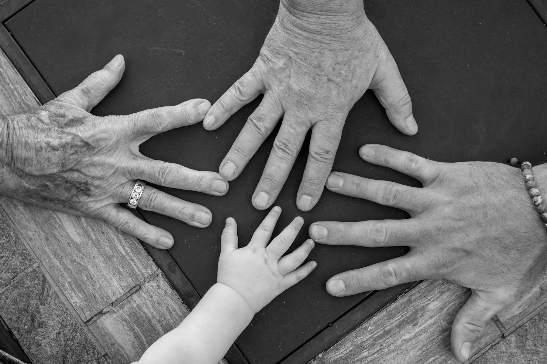 Las manos de tres generaciones —abuelos y un niño pequeño— formando un círculo sobre una mesa.