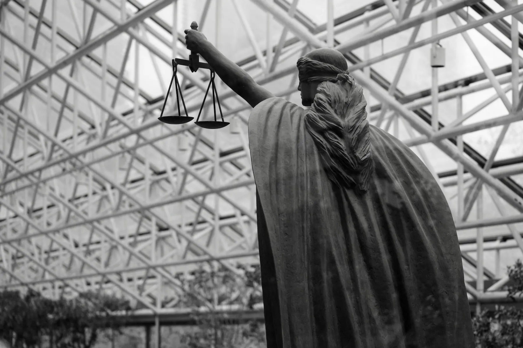 Una estatua de la justicia sostiene una balanza en blanco y negro, vista desde atrás.
