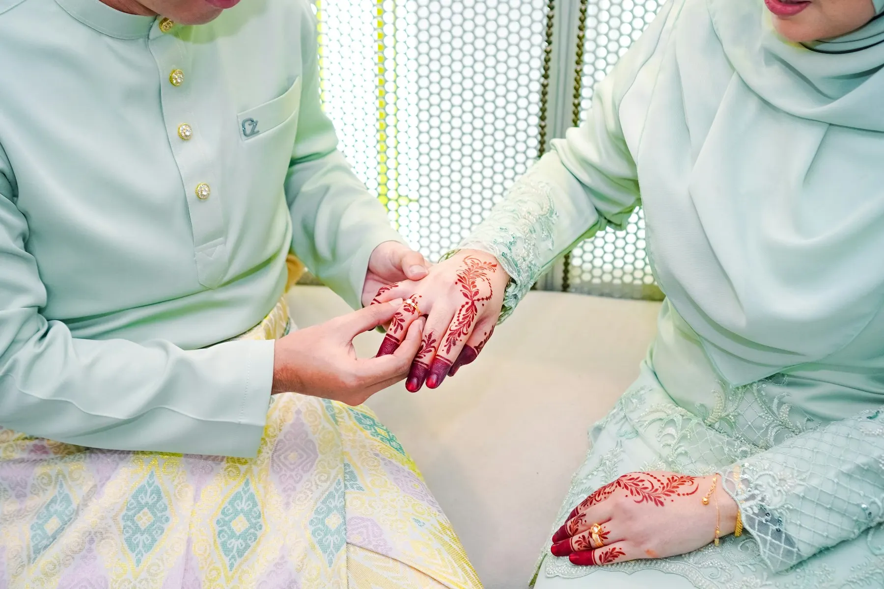 Una pareja musulmana sentada durante su nikah; él toma la mano de ella, vestida de blanco con hiyab.