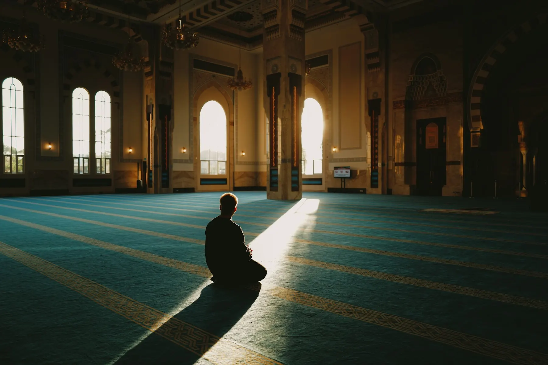 Un hombre reza solo en una mezquita, iluminado por un haz de luz que entra por la ventana.