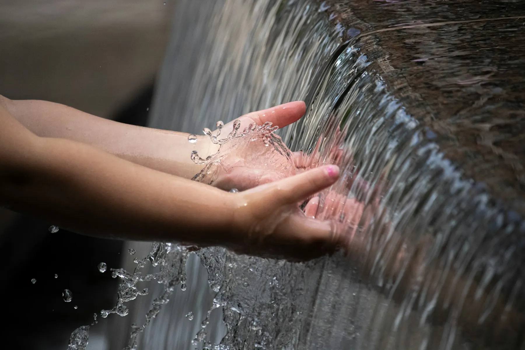 Dos manos recogen agua clara que cae de una fuente de ablución.