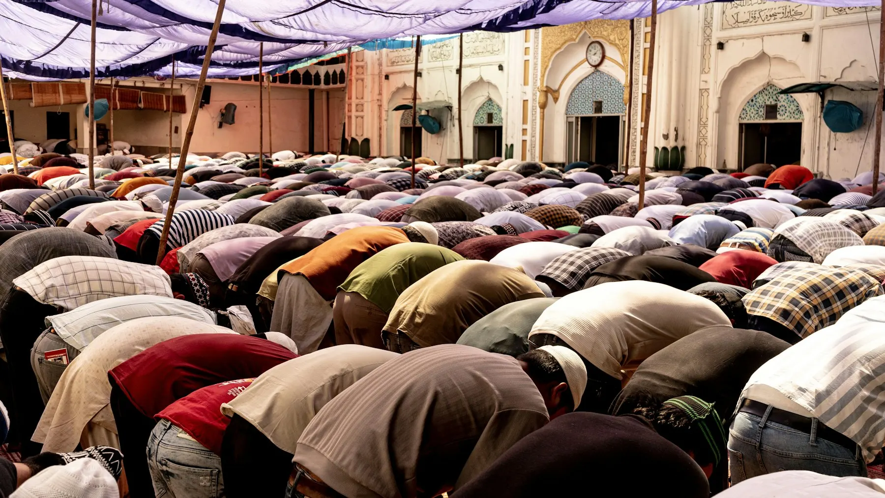 Una fila de personas descalzas rezando en una mezquita durante el sermón del viernes, vista desde atrás.